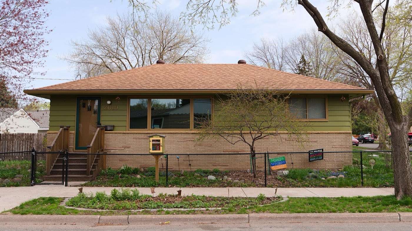 Single-story ranch house behind a low fence on a residential street